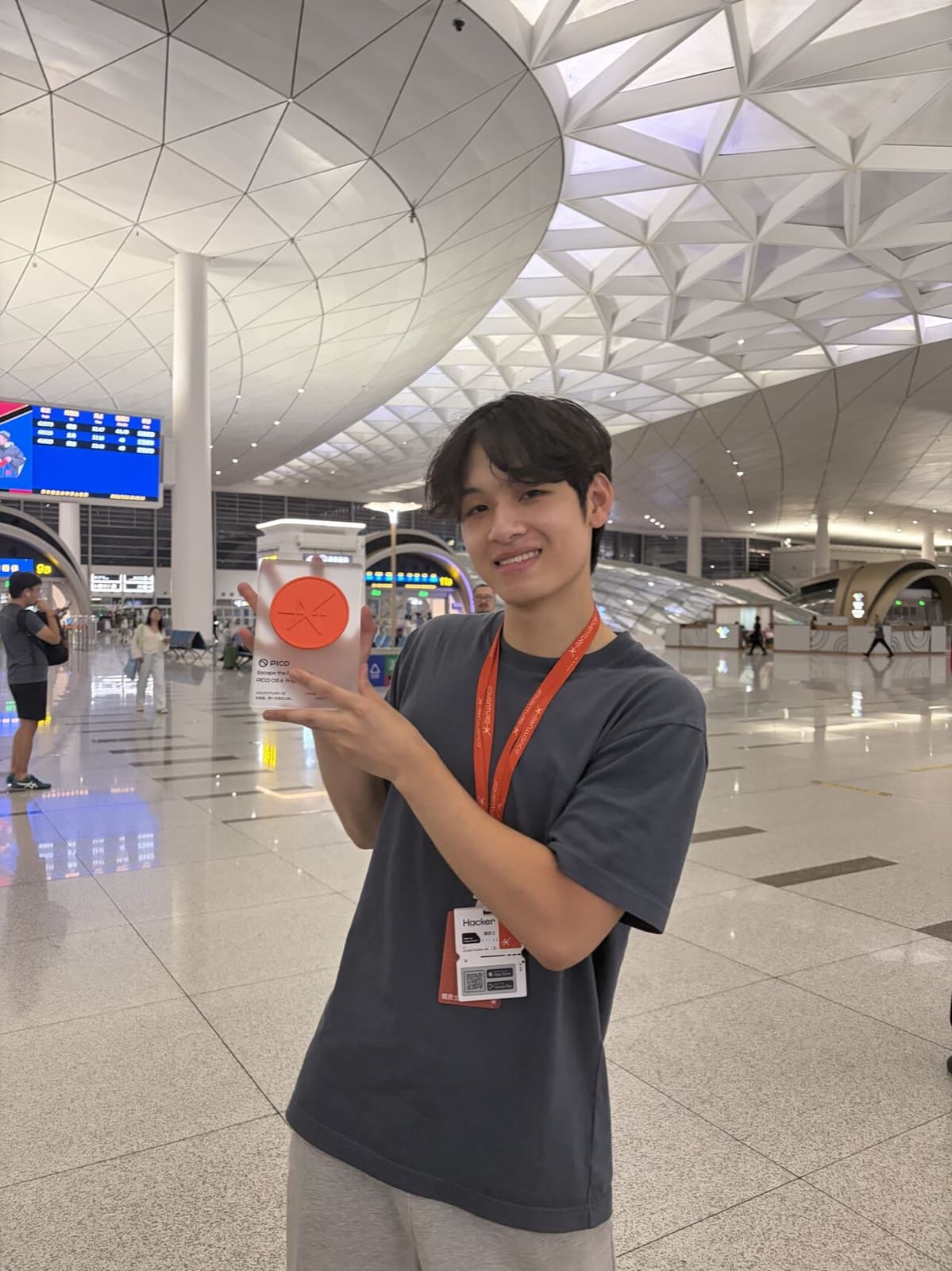 Nam holding the orange Pico track trophy at Hangzhou airport, lanyard still on