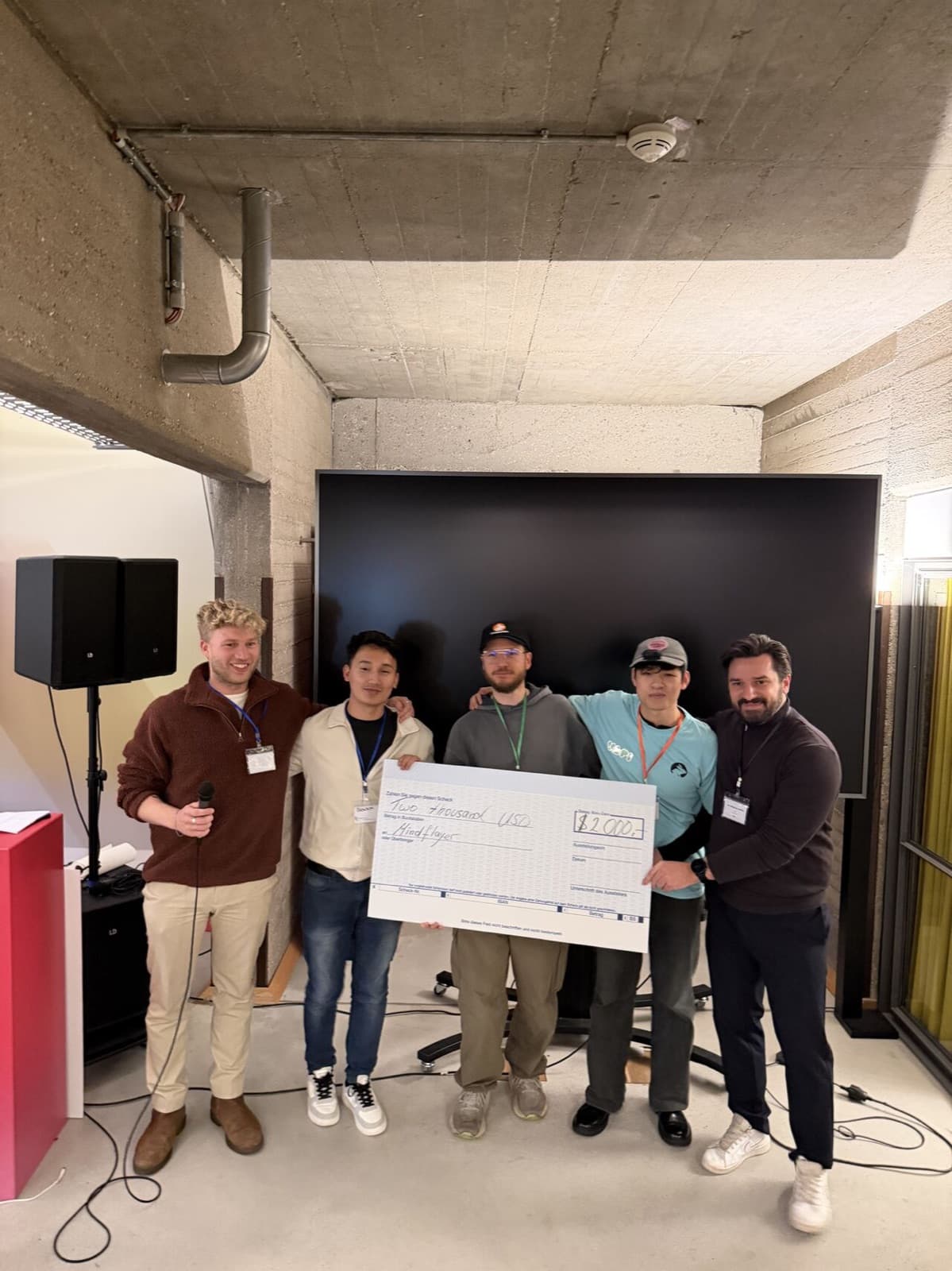 Team and organizers holding the AI Sprint winner cheque in a brick-walled venue